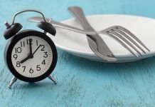 reloj, cubiertos y plato sobre una mesa escenificando el ayuno intermitente