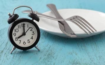 reloj, cubiertos y plato sobre una mesa escenificando el ayuno intermitente