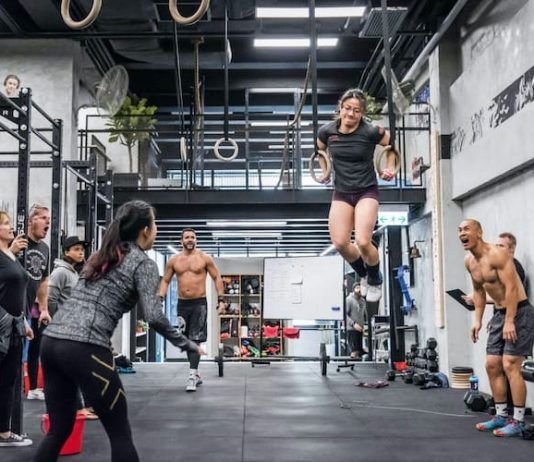 chica realizando ring muscle up en el box con atletas apoyando
